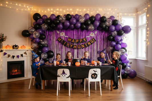 Purple and black Halloween balloon garland kit decorating a kids' party living room wall with fringe curtain backdrop