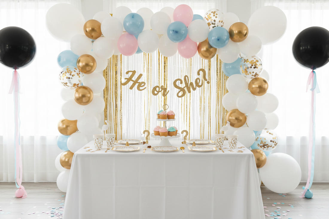 Gender reveal party decorations featuring balloon garland arch, fringe curtain backdrop, styled reveal table with He or She banner, and pink and blue confetti balloons